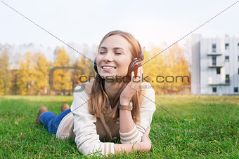 Student lying on grass and listening music into headphones