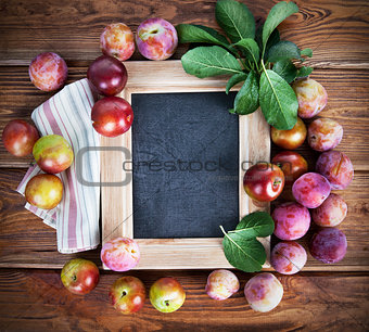 Board for text with fresh plums and green leaves