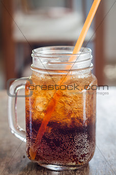 Glass of cola with ice on wooden table
