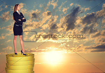 Businesswoman standing on coins stack
