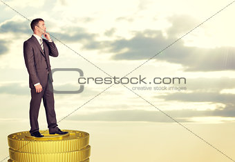 Thinking businessman standing on coins stack