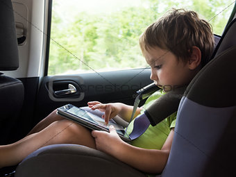 Little boy playing on computer tablet  in the car