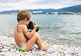 Little photographer with big camera on beach near sea