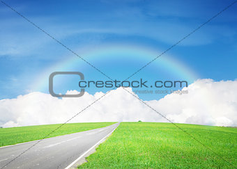 Asphalt road through the green field and sky with clouds and rai