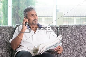 Indian man reading newspaper and calling phone