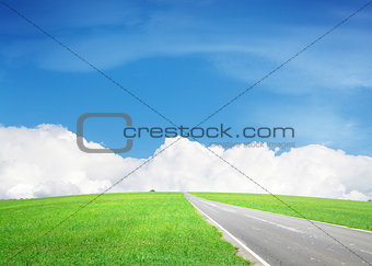 Asphalt road through the green field and sky with clouds