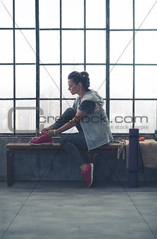 Fit woman sitting in profile in city loft gym tying shoe