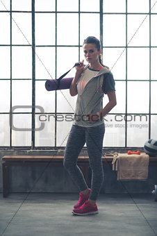 Serious woman in workout gear holding yoga mat in loft gym