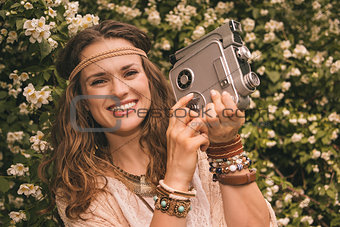 portrait of bohemian young woman among flowers with retro camera