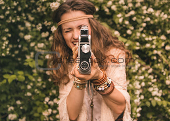 closeup on bohemian young woman among flowers using retro camera