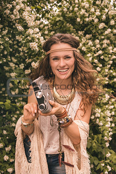 smiling hippie young woman among flowers with retro camera