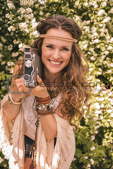 happy boho young woman among flowers with retro camera