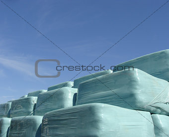 stack of hay in blue plastic wrap on a sunny day     