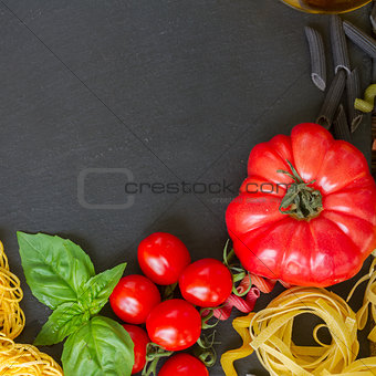 Raw pasta with ingridients on black board