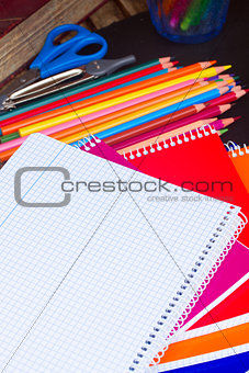 Empty notebook and set of colorful pencils on black board