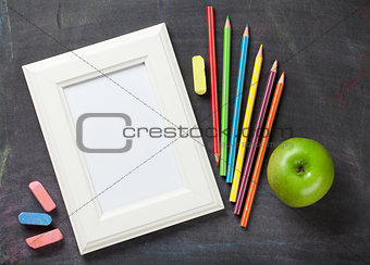 Photo frame and school supplies on blackboard background