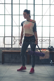 Woman standing in loft gym looking down holding yoga mat