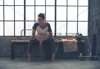 Woman resting elbows on knees while sitting on bench in loft gym