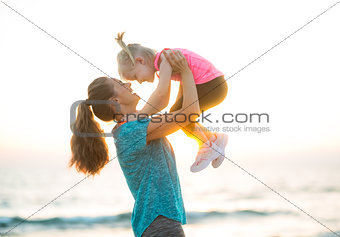Happy mother holding child up in air at the beach at sunset