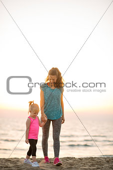 Fit young mother and daughter walking and holding hands on beach