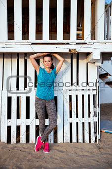 Fit woman standing in workout gear at a beach house
