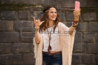 happy boho young woman near stone wall making selfie