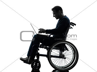 handicapped man computing laptop computer  in wheelchair silhoue