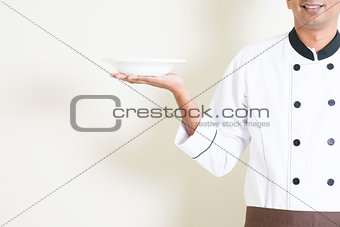 Indian male chef in uniform holding an empty plate