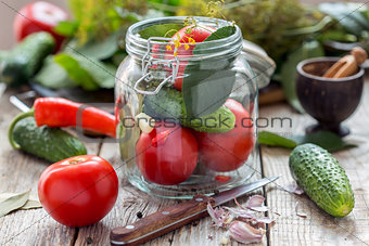 Vegetables and herbs in the glass jar on a wooden table.