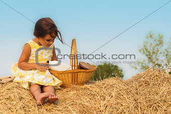 Little girl sitting on haystack with a basket of healthy food