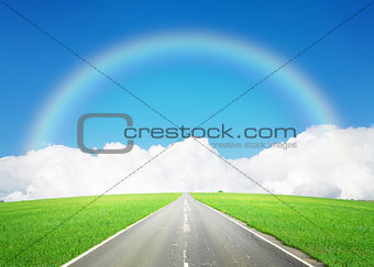 Road through the green field and sky with clouds and rainbow