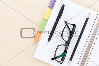 Office table with glasses over notepad, pen and pencil
