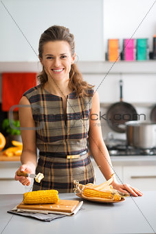 Elegant woman in kitchen smiling while putting butter on corncob
