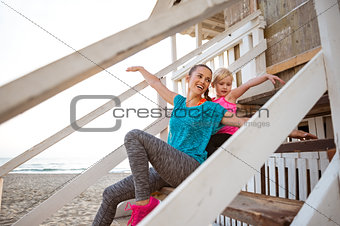 Mother and daughter sitting together at beach pretending to fly