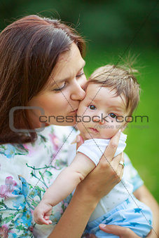Mother kisses baby son, close-up, summer