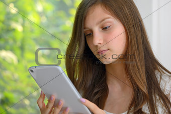 Serious young girl reading  on a tablet computer