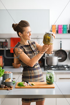 Smiling and elegant woman in kitchen holding up jar of pickles