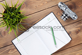 Office desk with calendar notepad, camera, supplies and flower