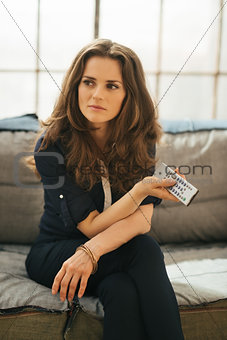 Woman with TV remote control relaxing on sofa in loft apartment