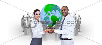 Composite image of business colleagues holding plant and looking at camera