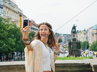 Hippie woman showing victory gesture and making selfie in Prague