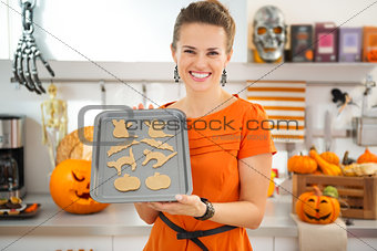 Happy housewife holding tray of uncooked Halloween biscuits