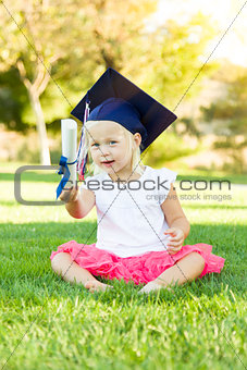 Little Girl In Grass Wearing Graduation Cap Holding Diploma With