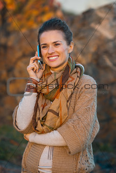 Woman talking mobile phone while walking in evening autumn park