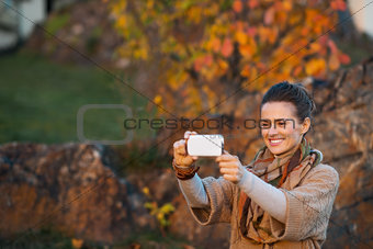 Woman taking photo with mobile while relaxing in autumn park