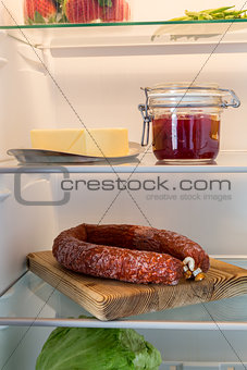 Open fridge stuffed with salami and foodstuffs