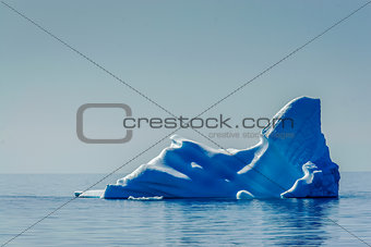 Lone, powerful blue iceberg floats on the still Arctic Ocean.