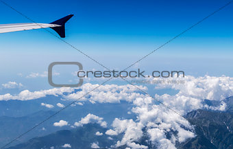 Wing of a Flying Airplane above clouds over Himalayan Mountains