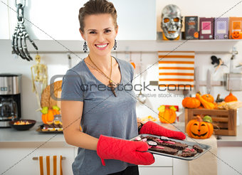 Smiling housewife holding tray with baked Halloween biscuits