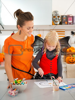 Mother with halloween dressed blond girl drawing Jack-O-Lantern